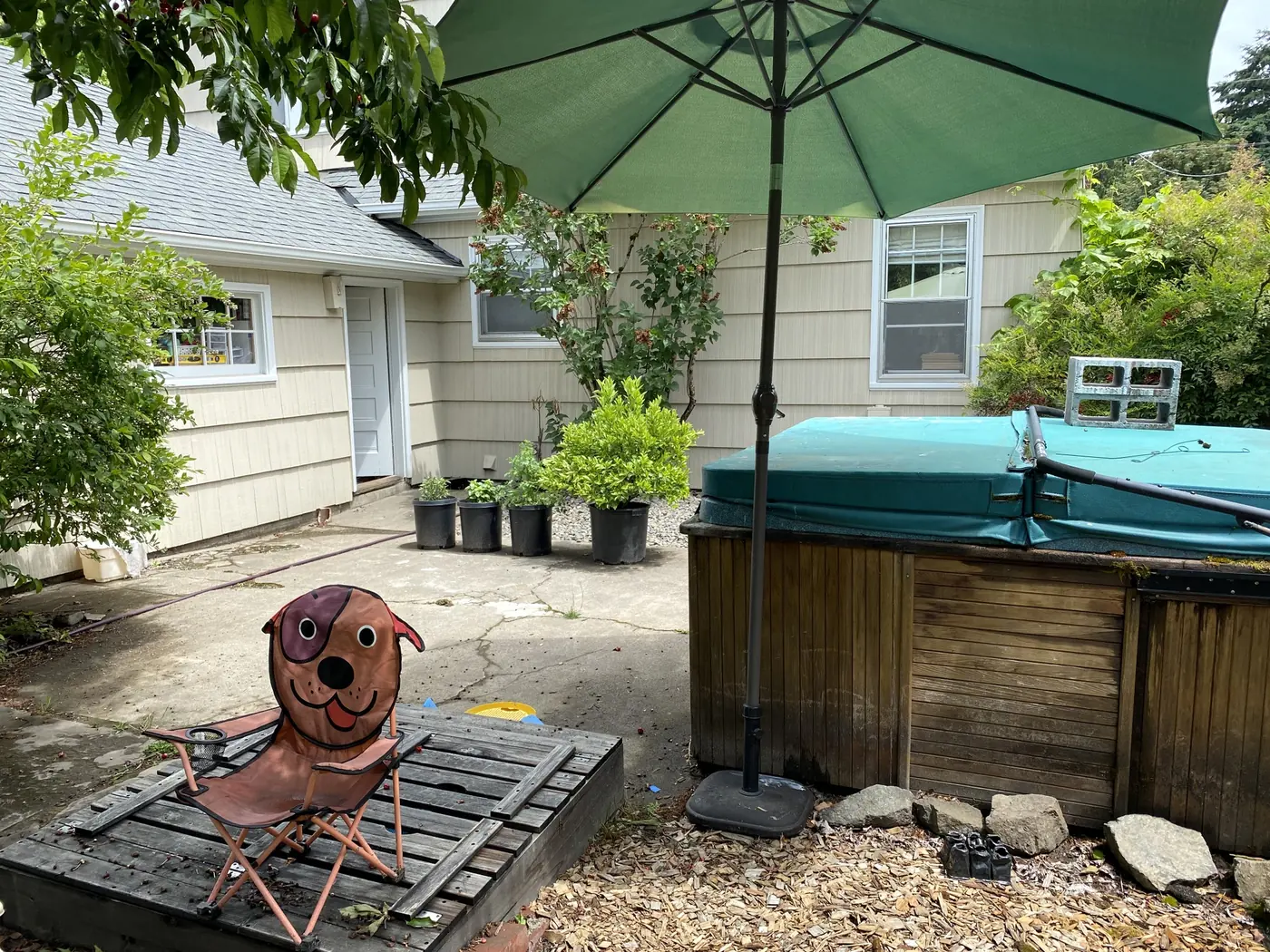 An old wood-sided hot tub under its cover in a backyard beside a patio umbrella