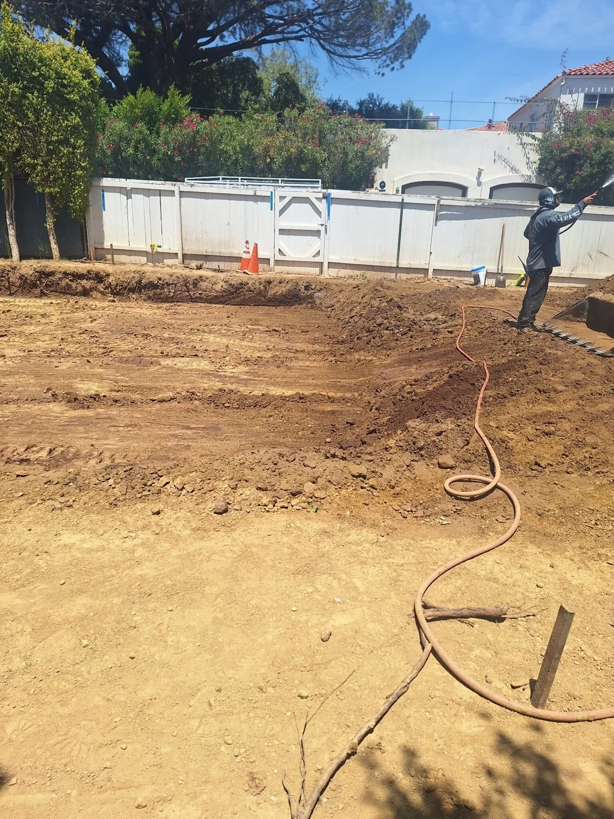 Crew member watering a graded yard for dust control during site work